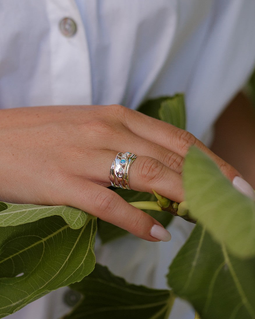 Hand wearing a silver ring with green leaves in the background