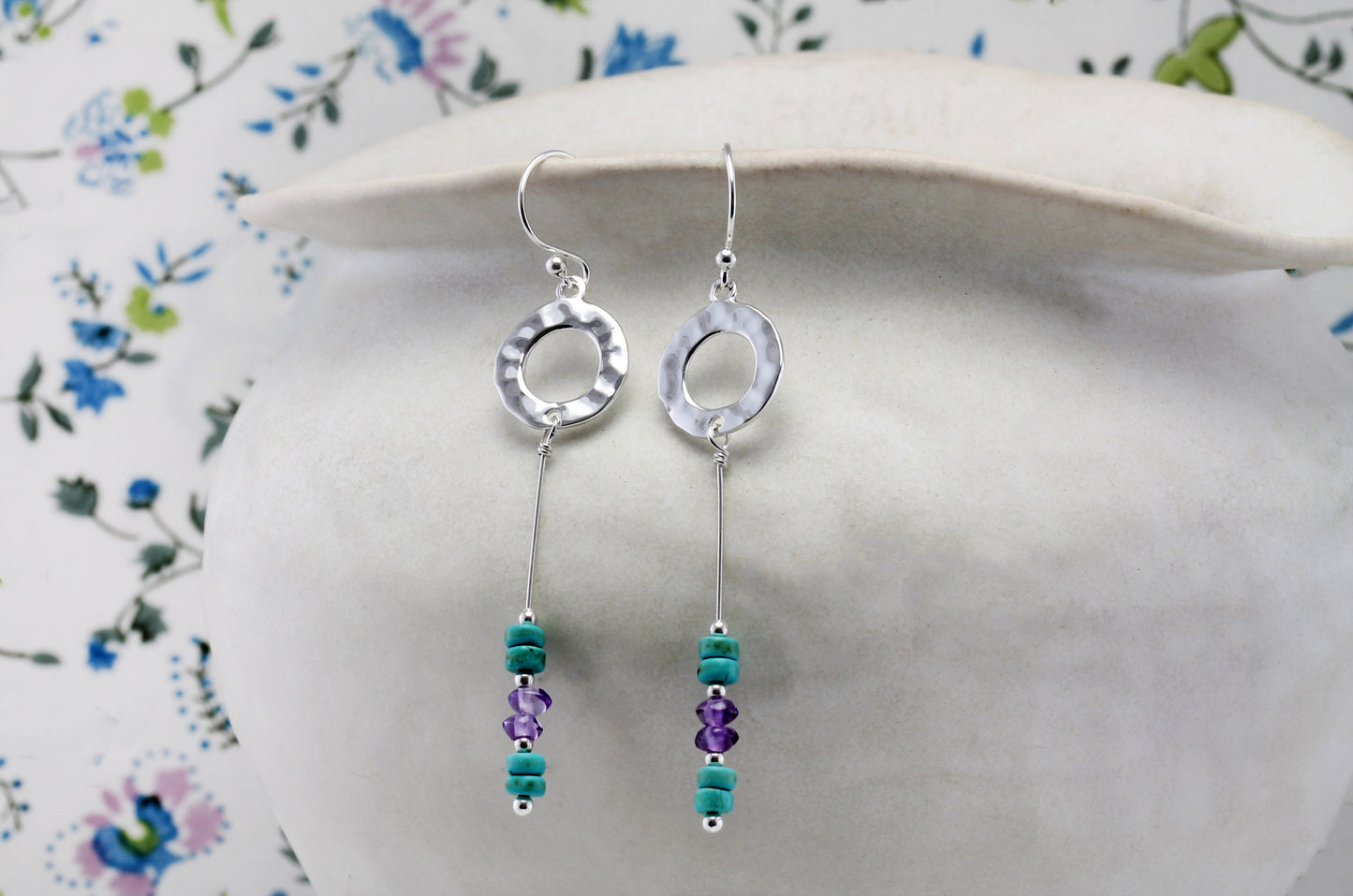 Hammered Circle Drop Earrings Turquoise & Amethyst Drop Earrings on a floral-patterned surface
