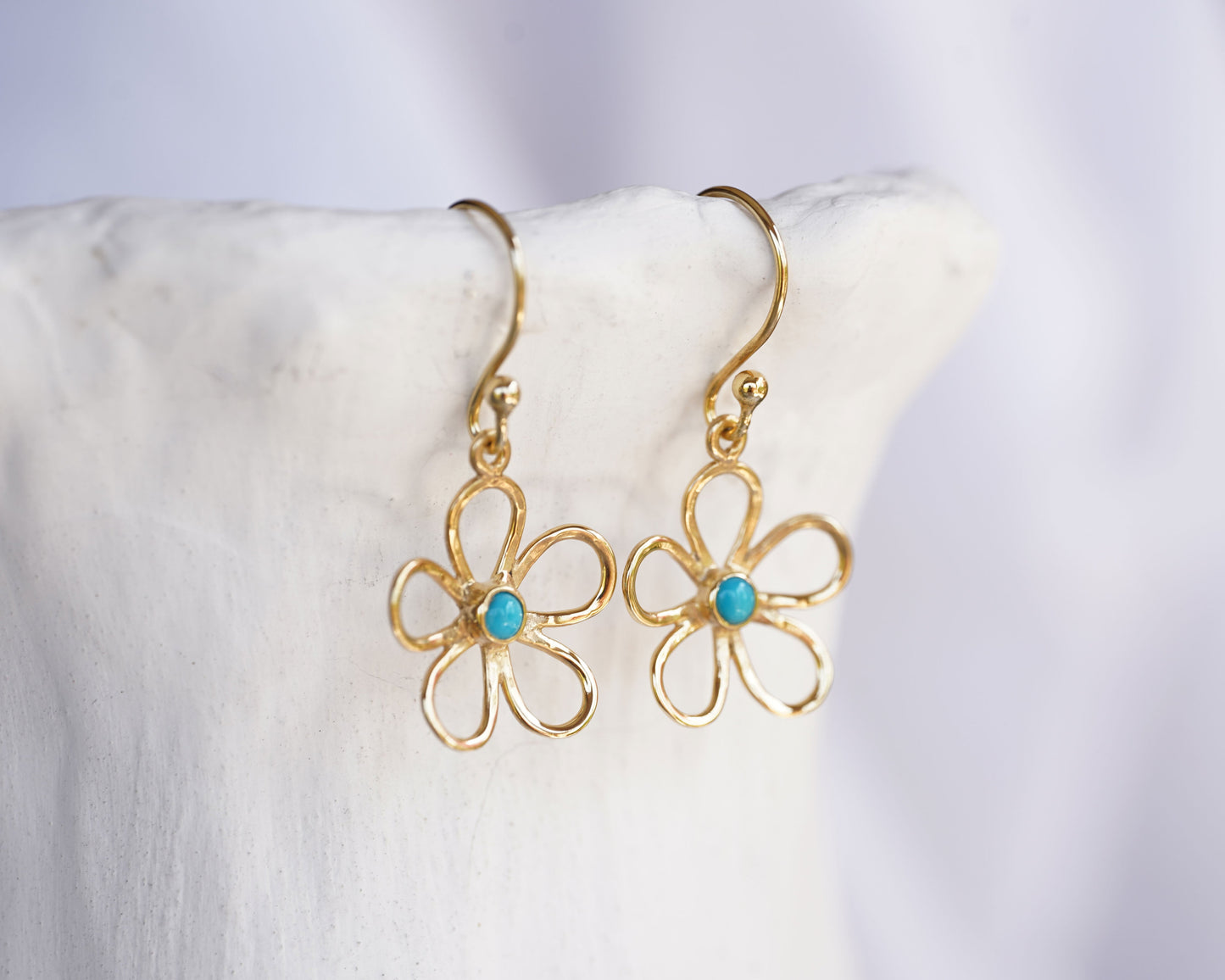 Gold flower-shaped earrings with turquoise stones on a white surface