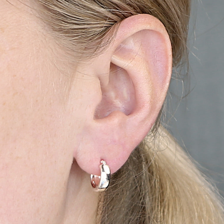Close-up of an ear wearing a gold hoop earring with a neutral background