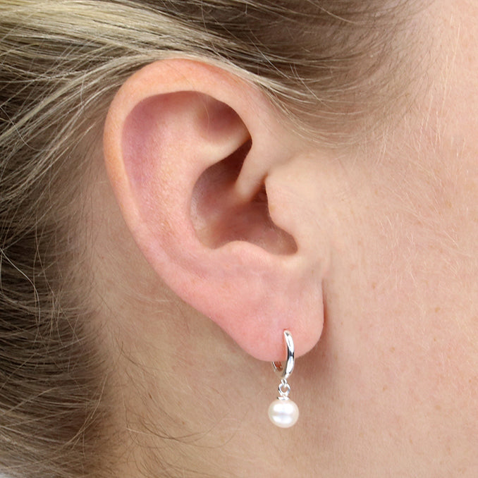 Close-up of an ear wearing a silver hoop earring with a pearl pendant.