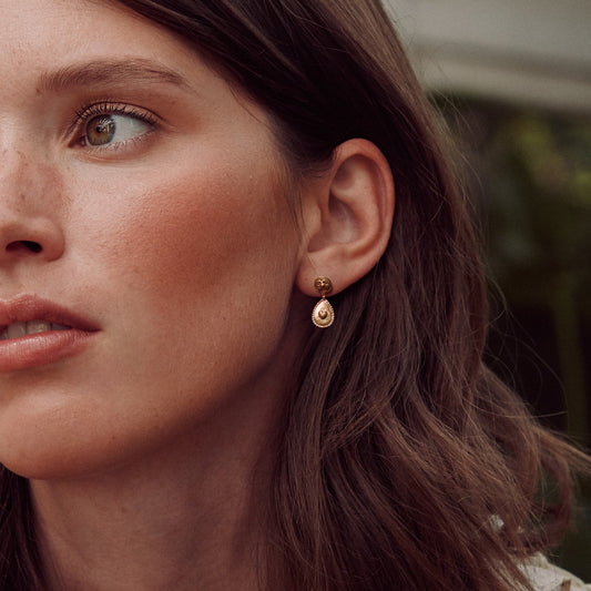 Close-up of a woman wearing Alex Monroe Silver & Gold Vermeil Love of Nature Heart & Flower Drop Earrings with a blurred background