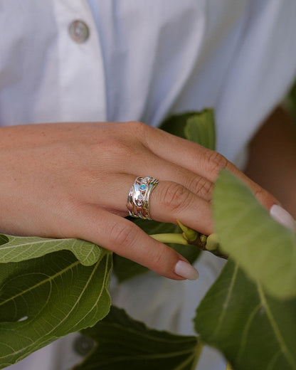 Hand wearing a silver ring with green leaves in the background