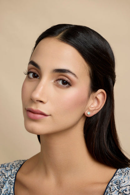 Woman with dark hair wearing Sterling Silver Emerald Stud Earrings With 14 carat Gold Detail against a beige background