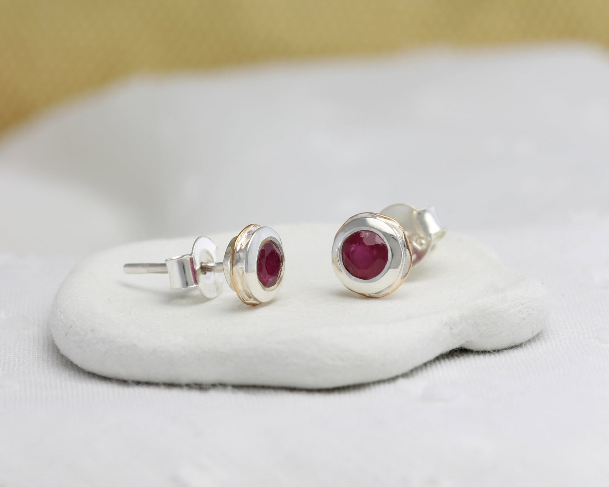 Sterling Silver Ruby & 14 carat Gold Detail Studs on a white cushion