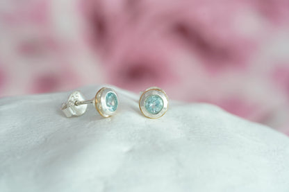 Pair of Sterling Silver Topaz With Gold Detail Studs on a white surface with a blurred pink background