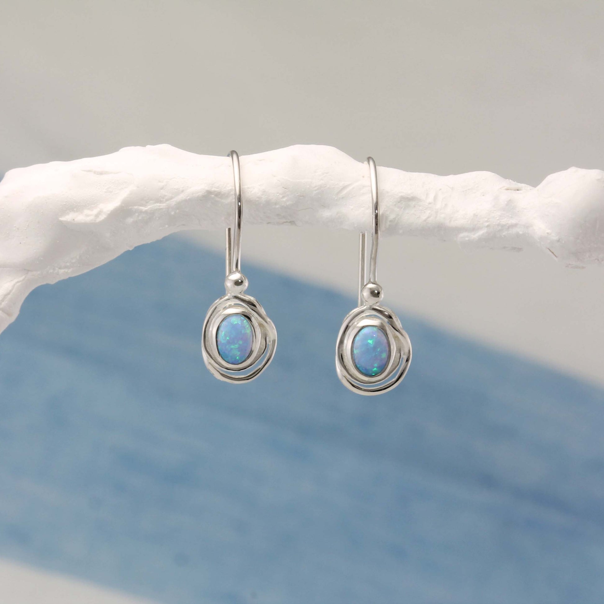 Sterling Silver Handmade Dainty Opalite Hook Earrings with opal stones on a white branch against a blue background