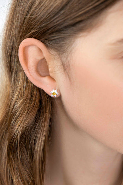 Close-up of an ear wearing a flower-shaped earring with a blurred background