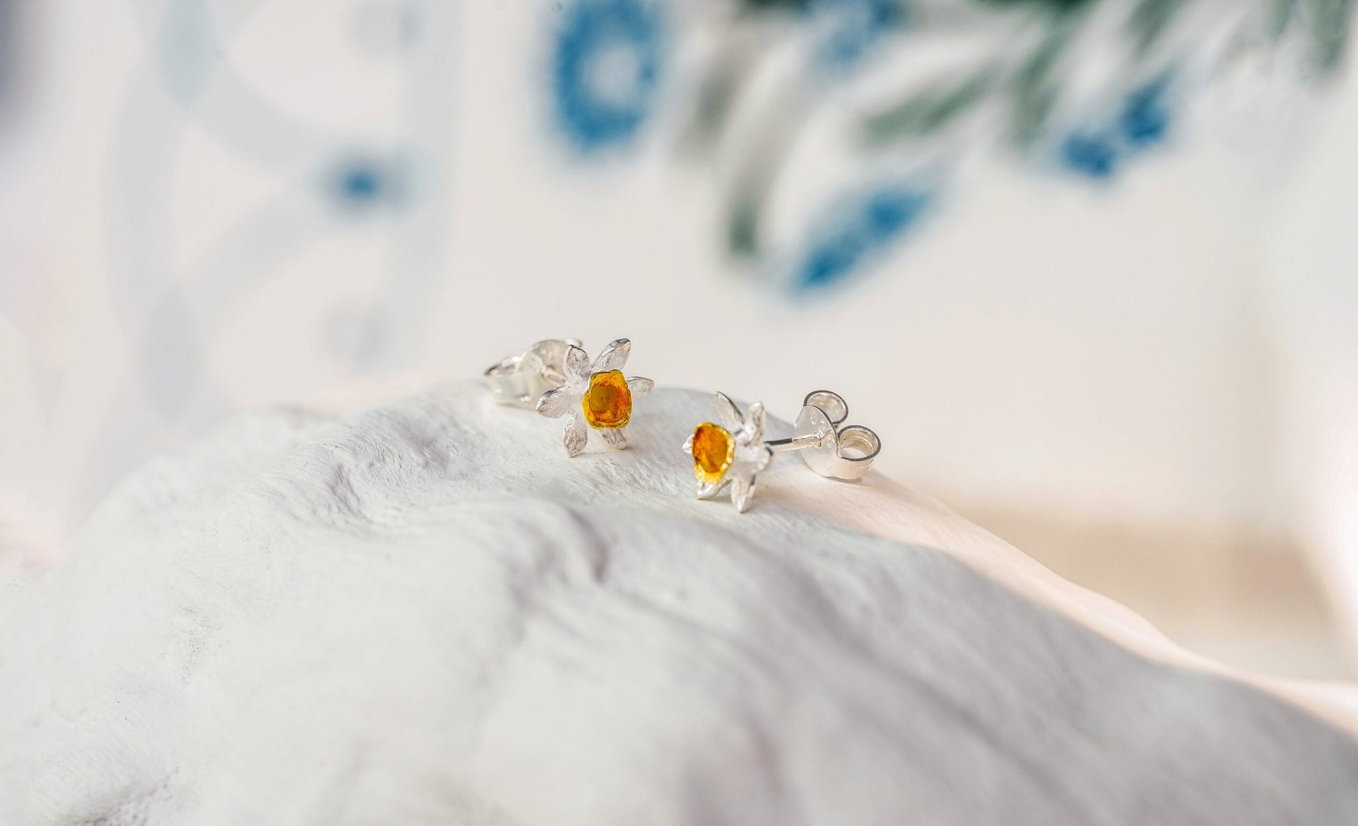 Pair of Sterling Silver & 18 carat Gold Vermeil Daffodil Studs with orange stones on a soft fabric background
