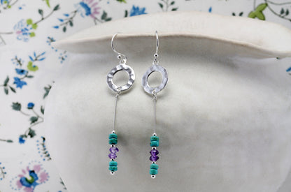 Hammered Circle Drop Earrings Turquoise & Amethyst Drop Earrings on a floral-patterned surface
