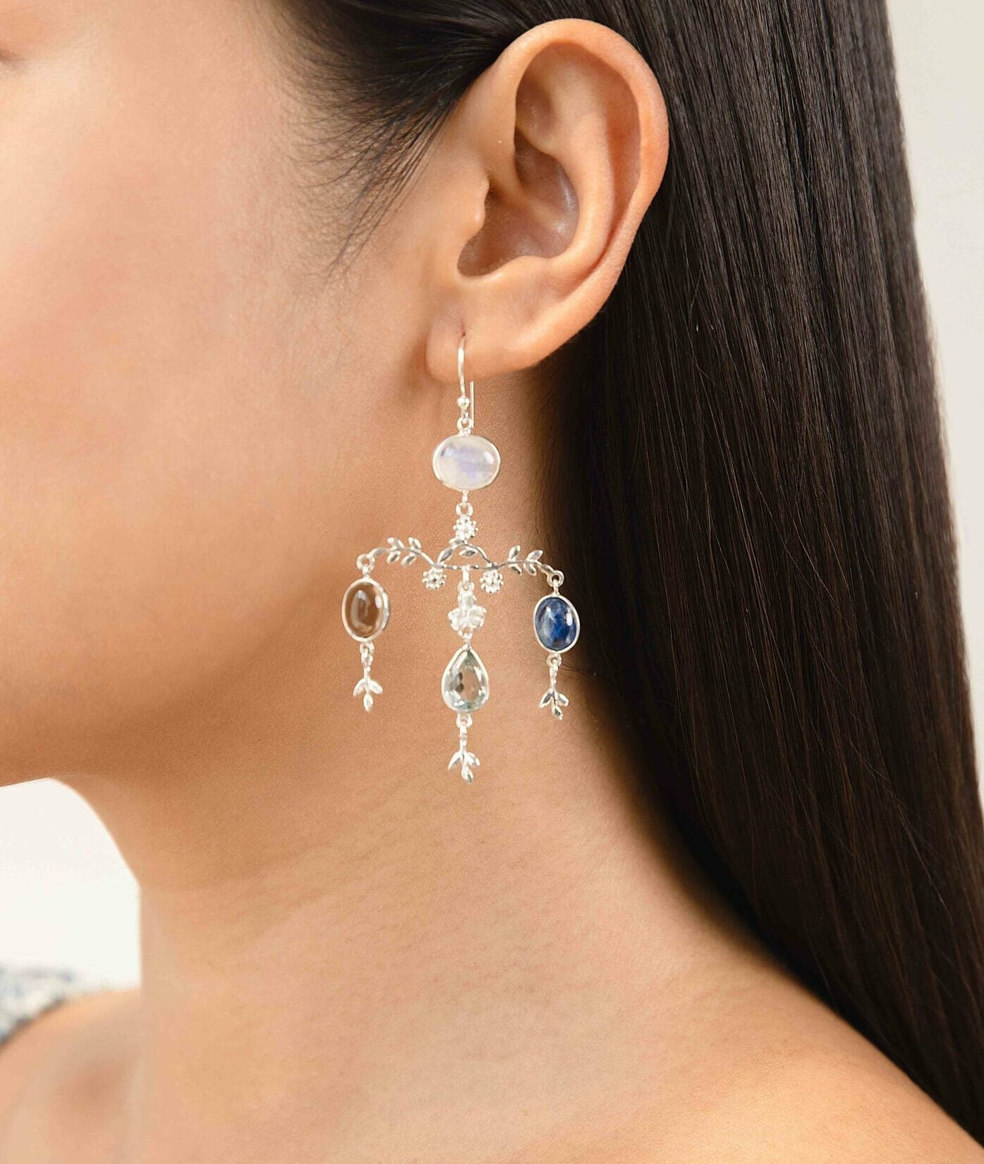 Close-up of a woman wearing a Sterling Silver Chandelier Gemstone Statement Earrings earring with gemstones against a neutral background