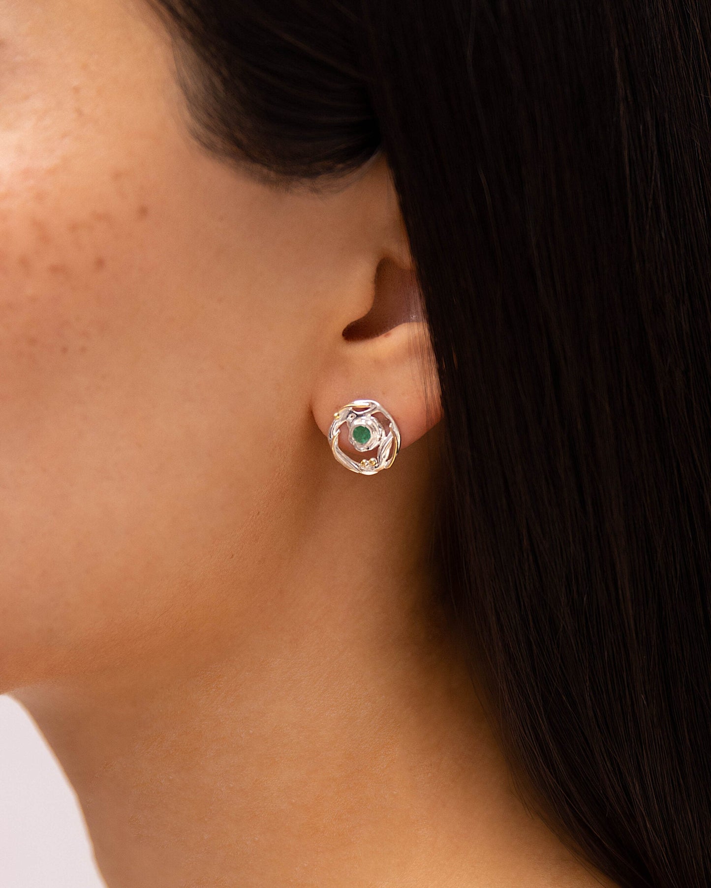 Close-up of a person wearing a sSterling Silver Circular Mixed Metal Round Emerald Stud Earring