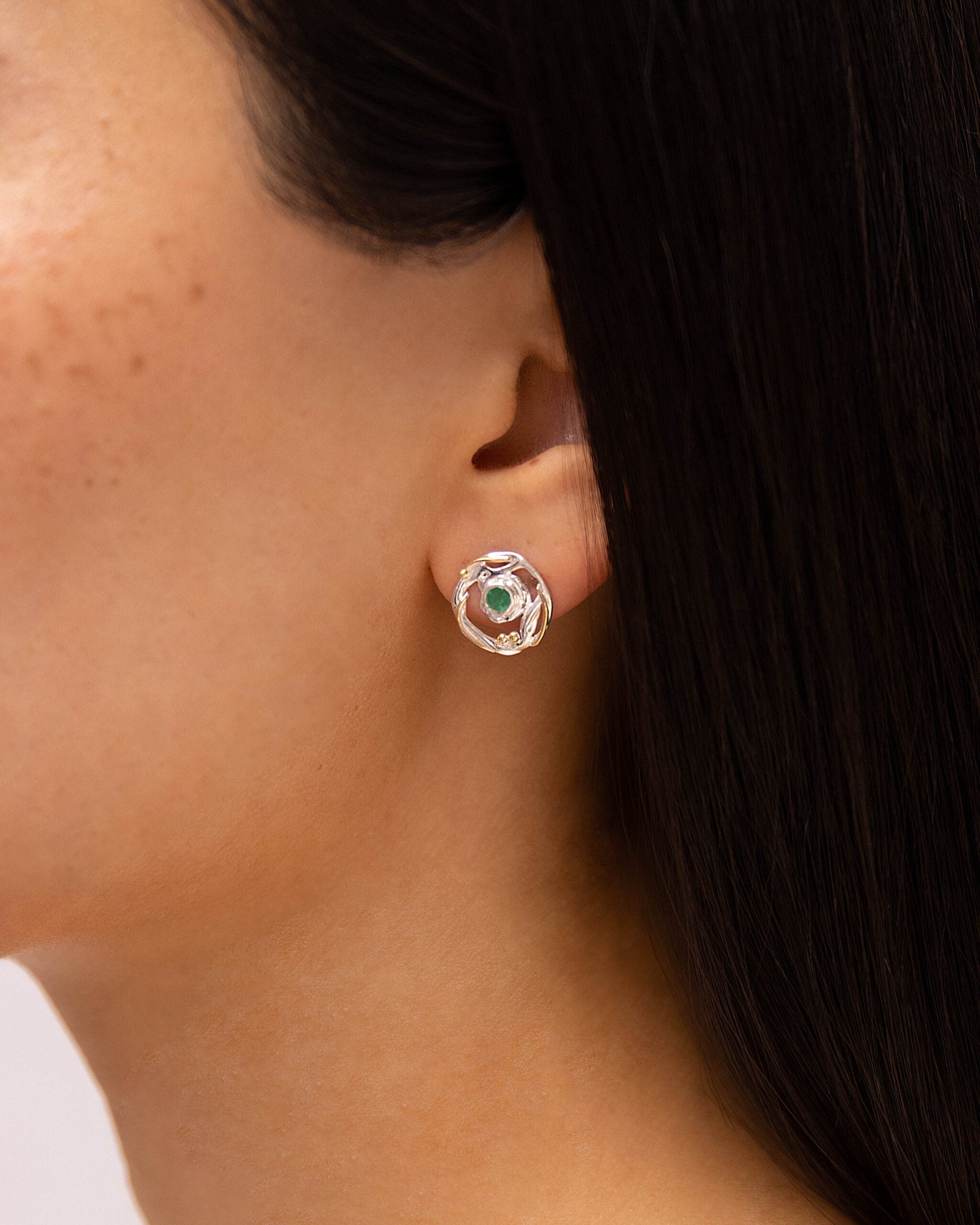 Close-up of a person wearing a sSterling Silver Circular Mixed Metal Round Emerald Stud Earring