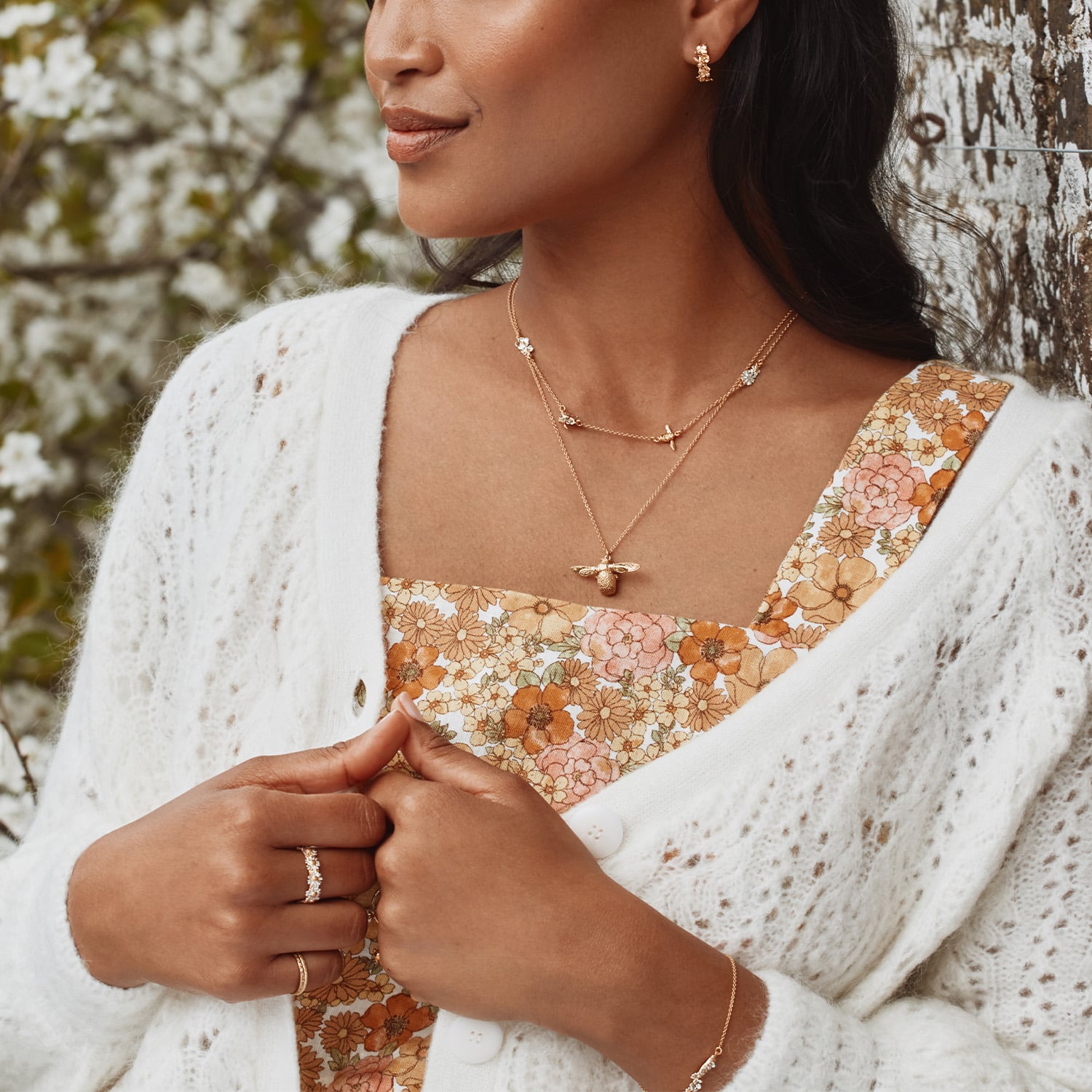 Woman wearing a floral dress and white cardigan with jewelry in a natural setting