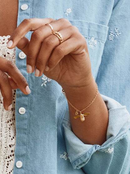 Close-up of a hand wearing gold rings and a Alex Monroe 22 carat Yellow Gold Vermeil Baby Bee Bracelet with a blue denim shirt in the background