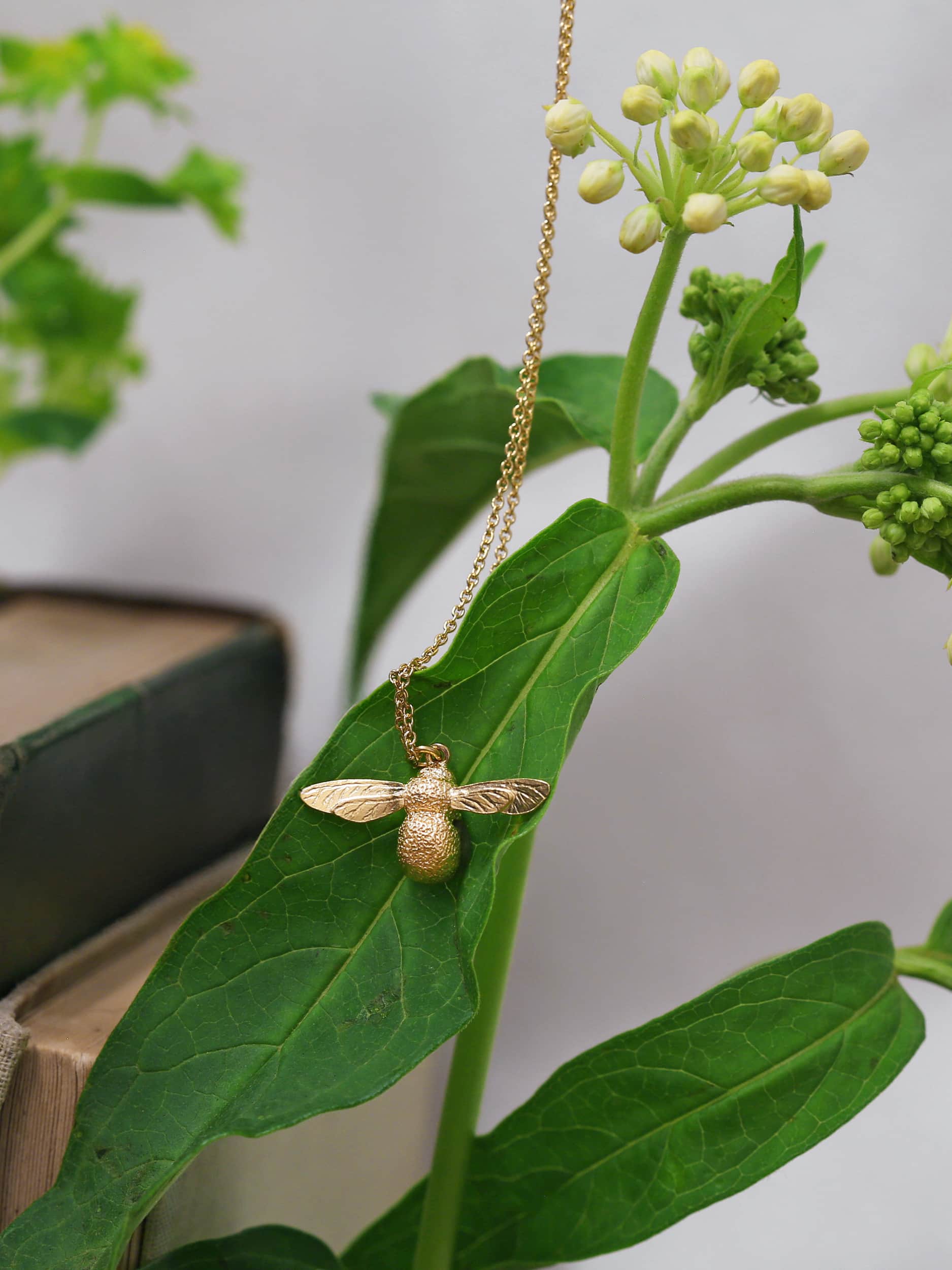 Alex Monroe Silver Gold Vermeil Baby Bee Necklace hanging on the green leaf of a plant