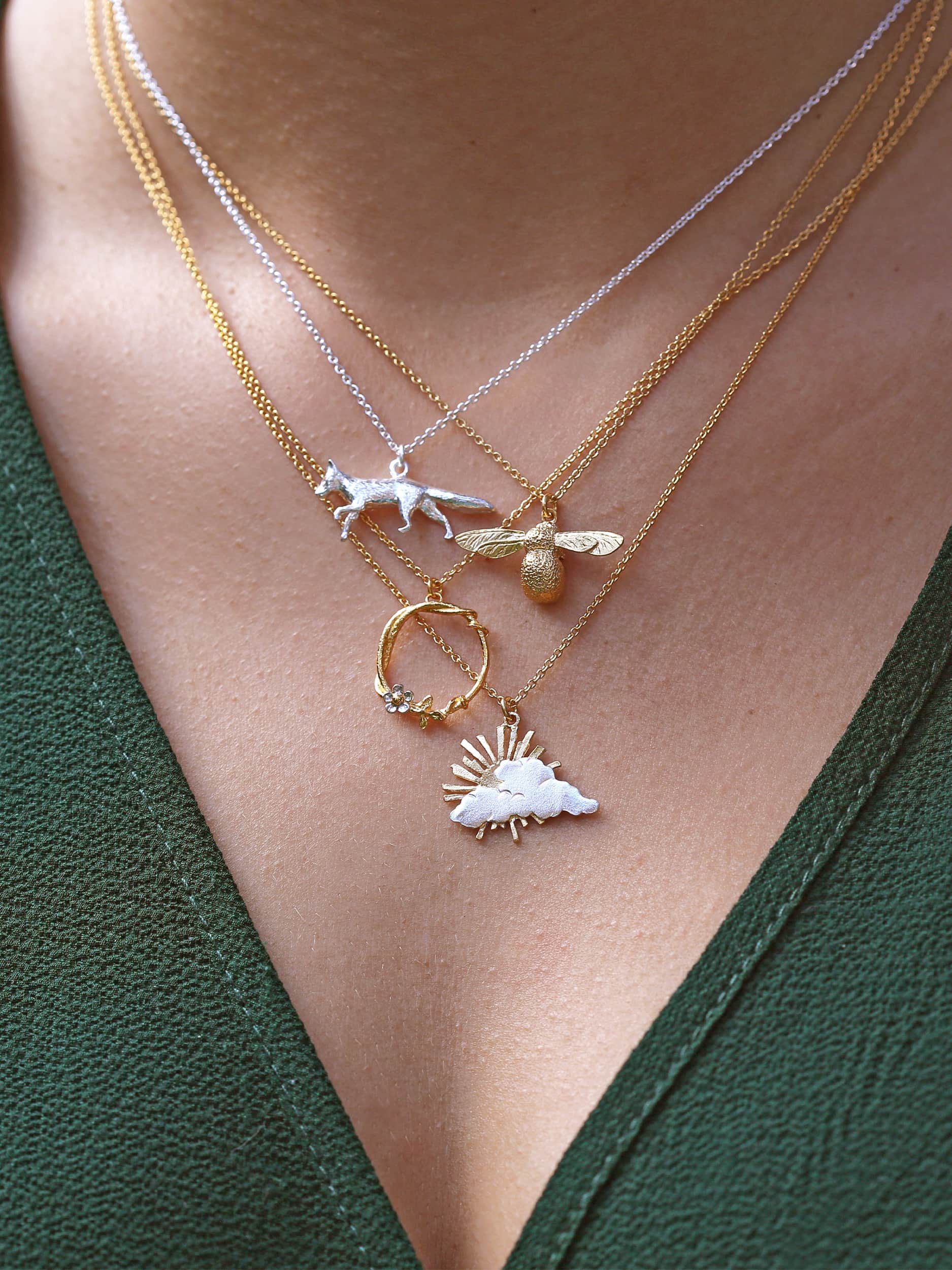 Three necklaces with various pendants on a person wearing a green top.