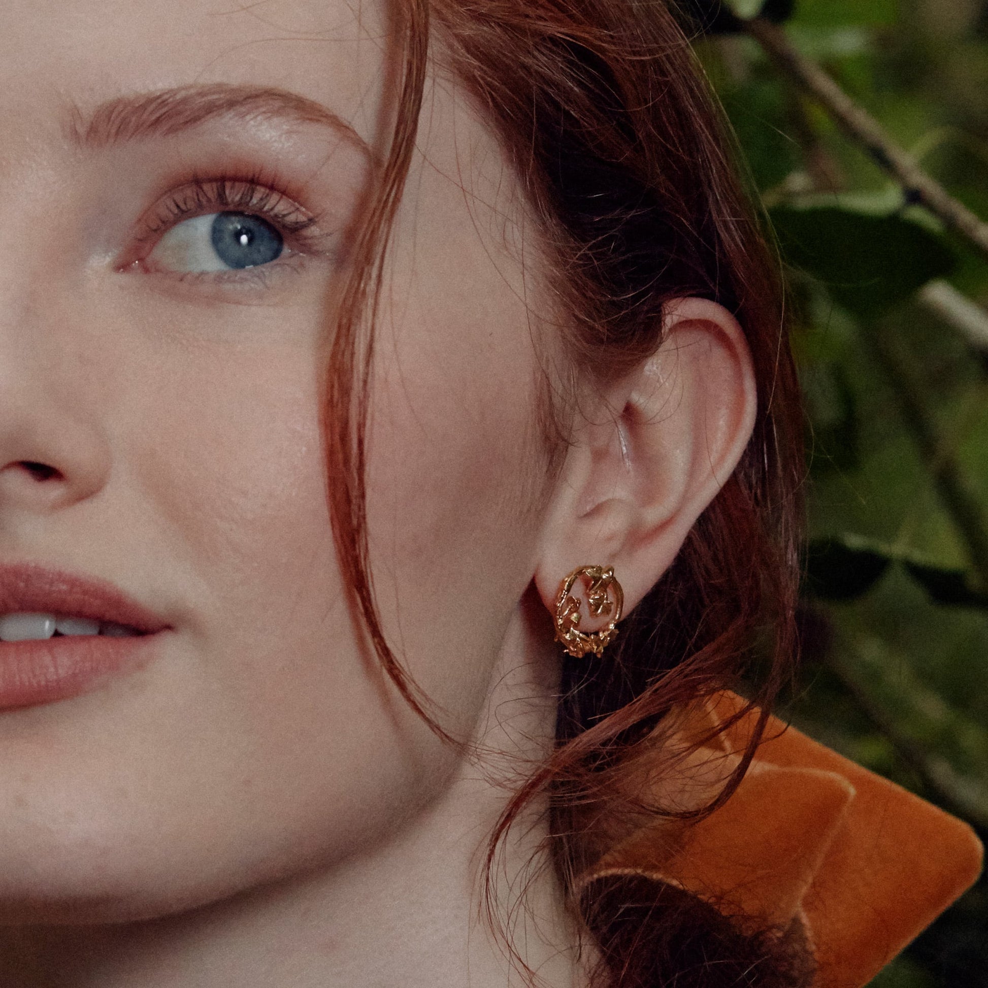Close-up of a woman wearing a gold Vermeil Woodland Loop Stud Earring with a blurred green background