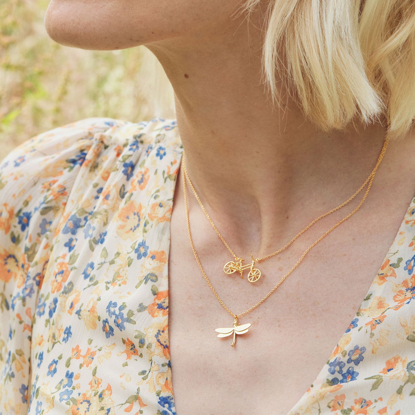 Woman wearing two gold necklaces with a floral patterned top