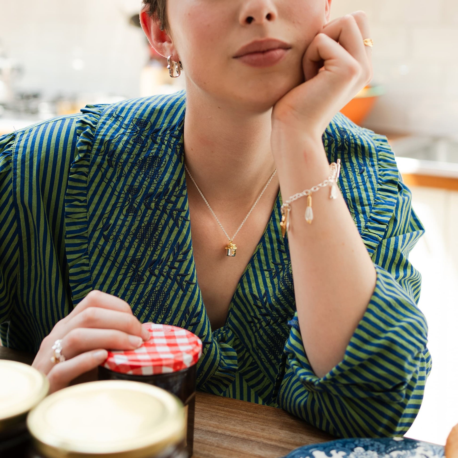 Woman sitting at a table wearing a Alex Monroe Silver & Gold Vermeil Marmalade Jar Necklace with a blurred background