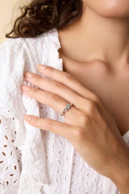 Close-up of a hand wearing a Dainty Sterling Silver open heart set with a blue opaline stone and a flower next to the heart with a white lace garment in the background