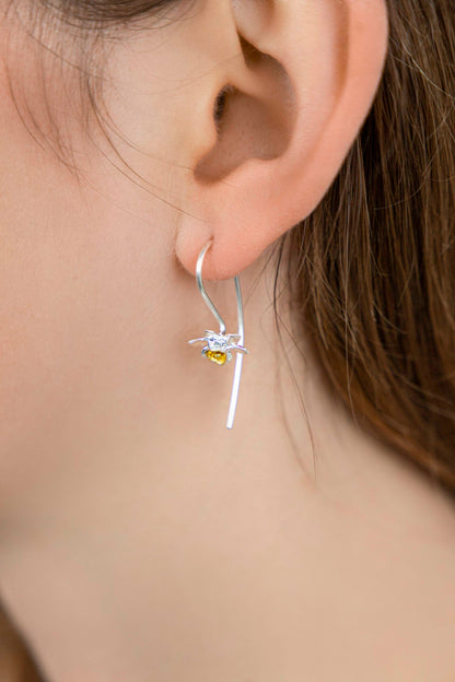 Close-up of a person wearing a silver earring with a yellow gemstone.