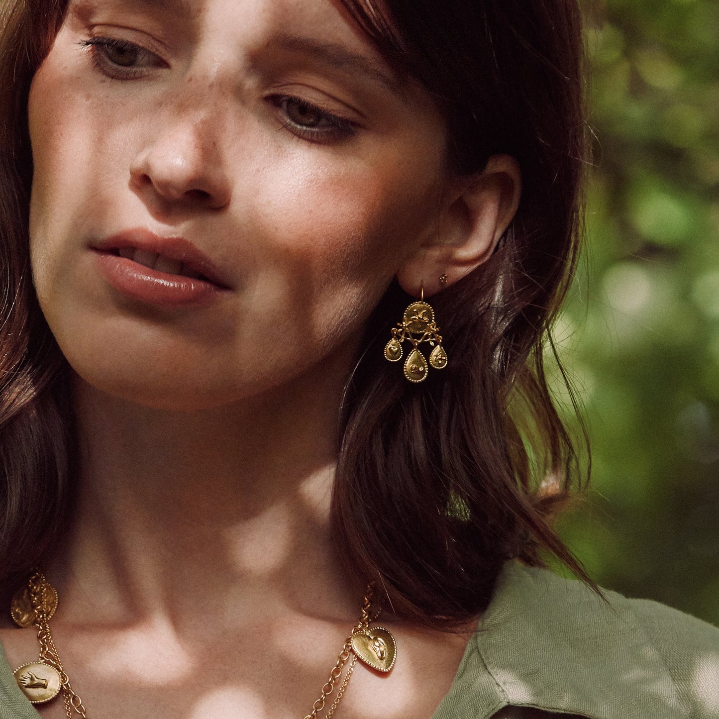 Woman wearing Alex Monroe Sterling Silver & Gold Vermeil Gratitude for Nature Girandole Earrings and a necklace with a blurred green background